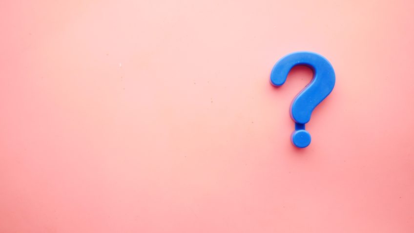 A plastic blue question mark on a pink wall surface.