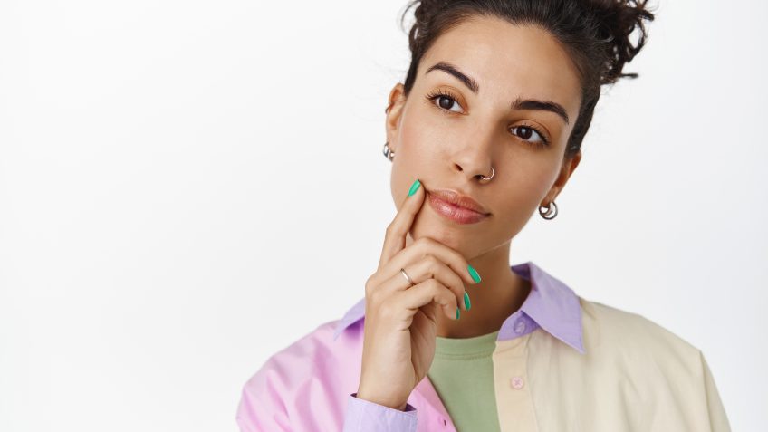 Thoughtful brunette girl making choice, looking at logo with ponder, touch face and thinking, standing against white background